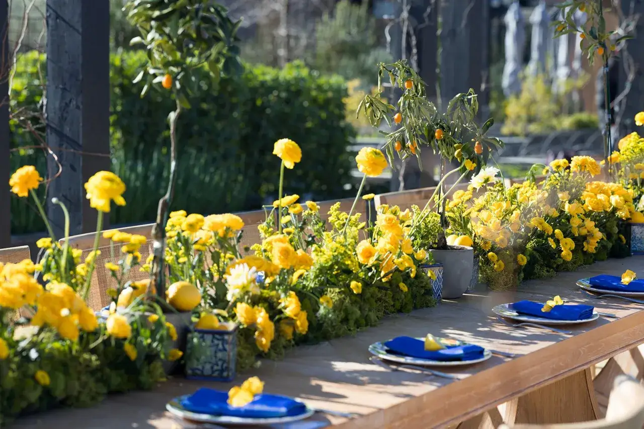 Une table dress&eacute;e pour un repas en plein air, orn&eacute;e d'une abondance de fleurs jaunes vives et de kumquats. Une deco table nature chic qui invite &agrave; la d&eacute;tente.