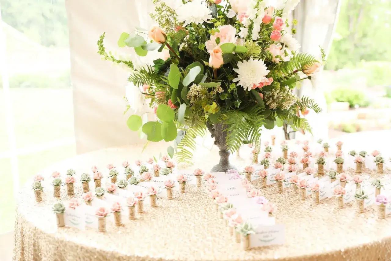 Marque place fleur, petits cactus et roses en tissu sur une table recouverte d'une nappe &agrave; paillettes dor&eacute;es, devant un bouquet de fleurs.