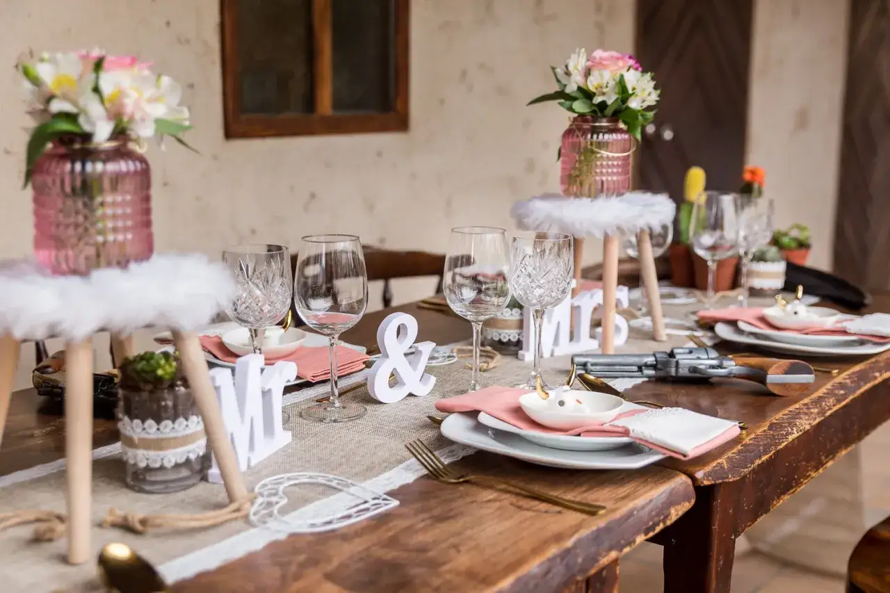 Table dress&eacute;e pour un mariage western : verres, fleurs roses, et un pistolet d&eacute;coratif.