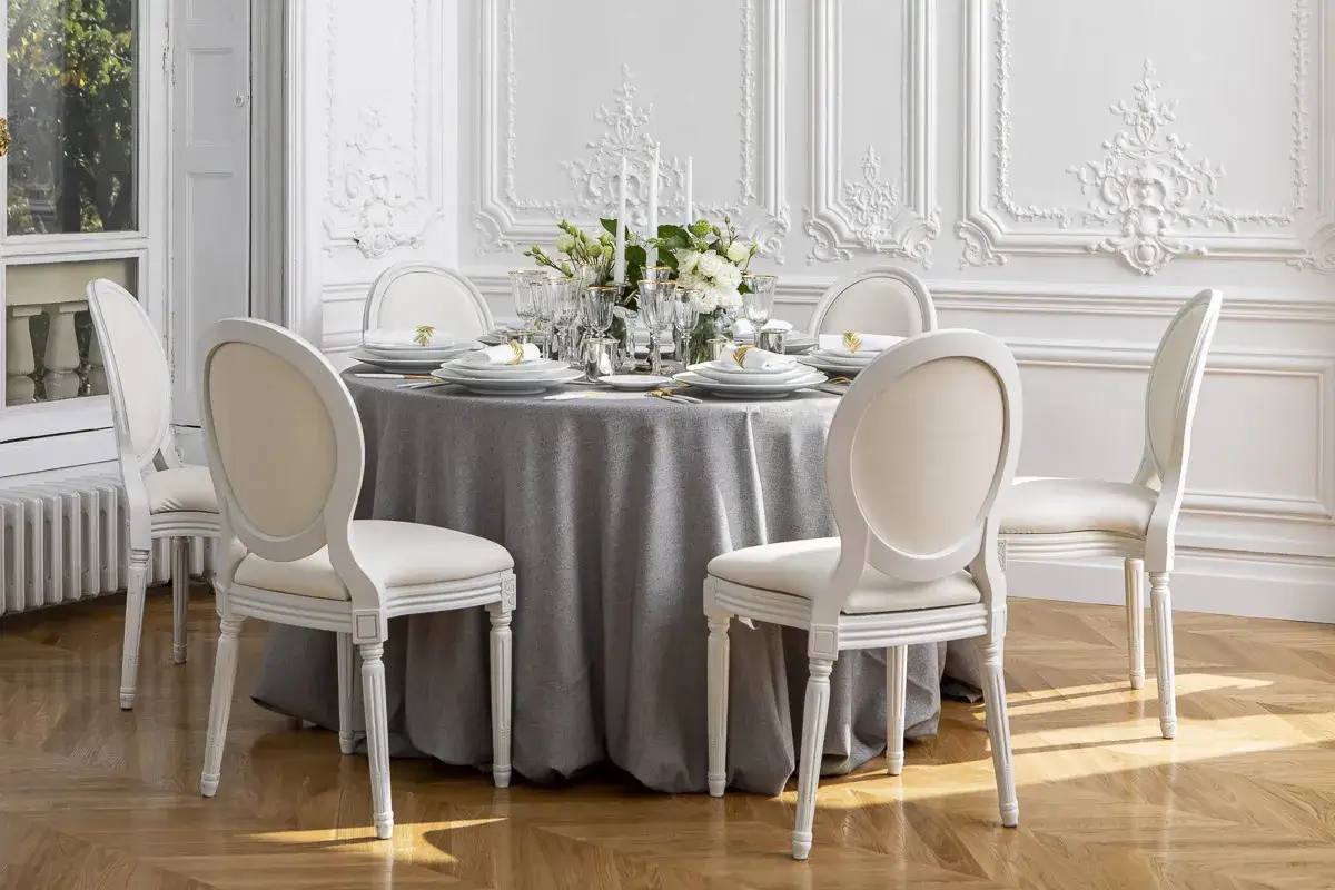 Une table &eacute;l&eacute;gamment dress&eacute;e avec une nappe grise, des chaises blanches et des fleurs. Quel nappe choisir pour une ambiance chic ?