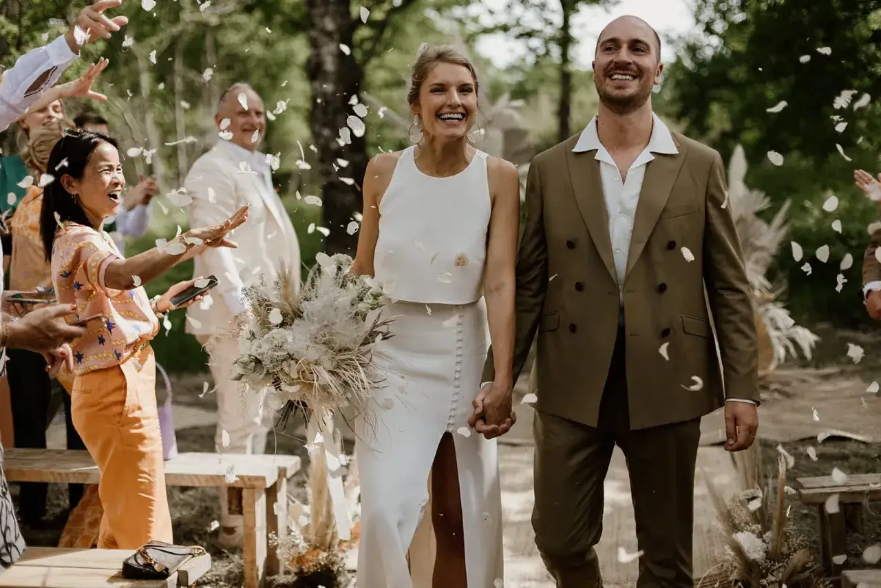 Un couple rayonnant, tel un po&egrave;me mariage Baudelaire, traverse une pluie de p&eacute;tales. Le mari&eacute; en costume vert, la mari&eacute;e en blanc, entour&eacute;s de joie.