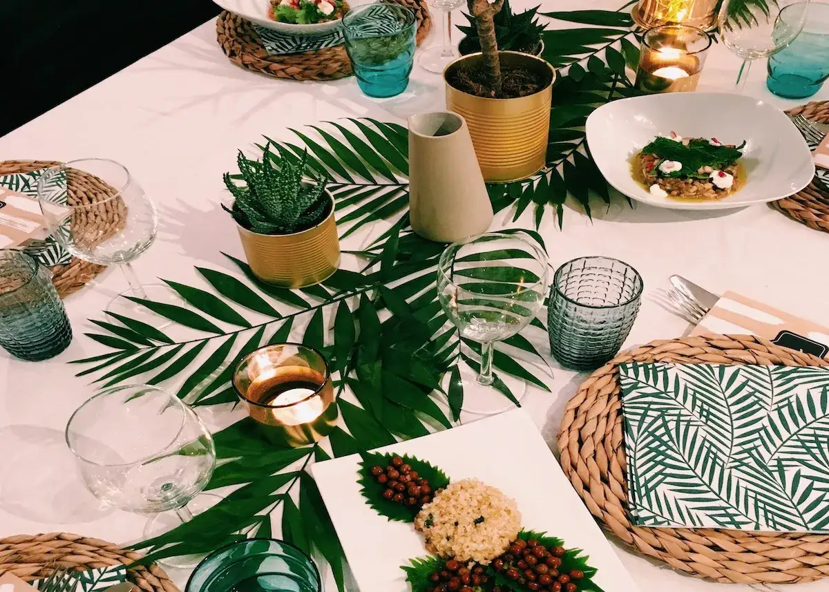 Une table dress&eacute;e dans une ambiance jungle, avec des feuilles de palmier, des plantes en bo&icirc;tes et des bougies.