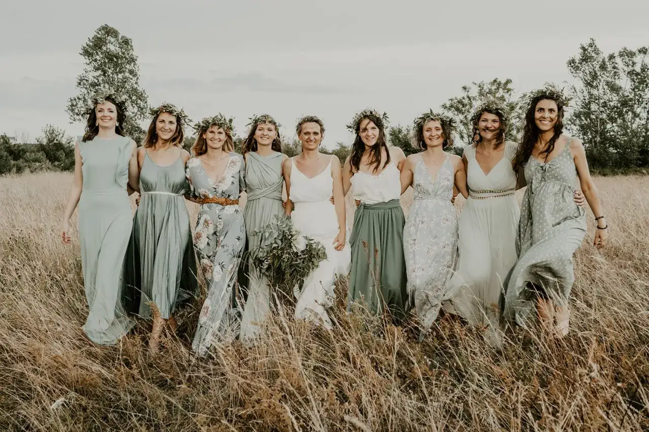 Un groupe de femmes souriantes, parées de couronnes de verdure, incarne le thème campagne chic dans une prairie dorée.