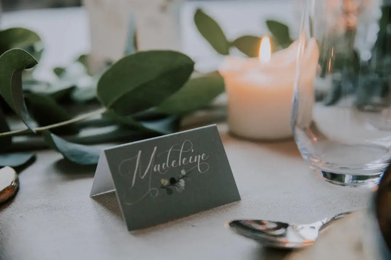 Un porte nom original &agrave; faire soi-m&ecirc;me, orn&eacute; d'une calligraphie &eacute;l&eacute;gante et d'une touche florale, sur une table dress&eacute;e avec des bougies et des feuilles vertes.