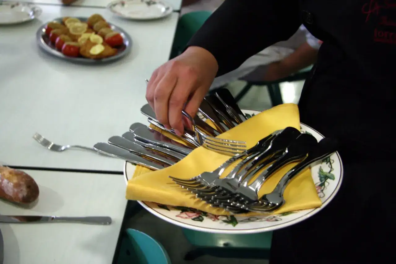 Une main saisit une fourchette à la française sur une assiette garnie de couverts.