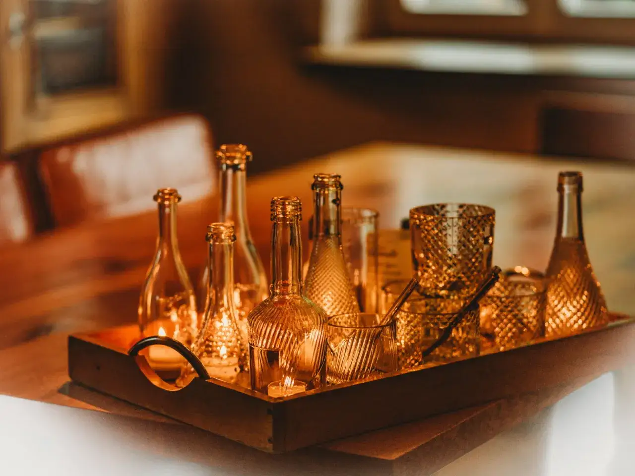 Sur un plateau en bois, des bouteilles et verres en verre ambr&eacute;, certains orn&eacute;s de motifs, &eacute;voquent la diff&eacute;rence entre verre et cristal.