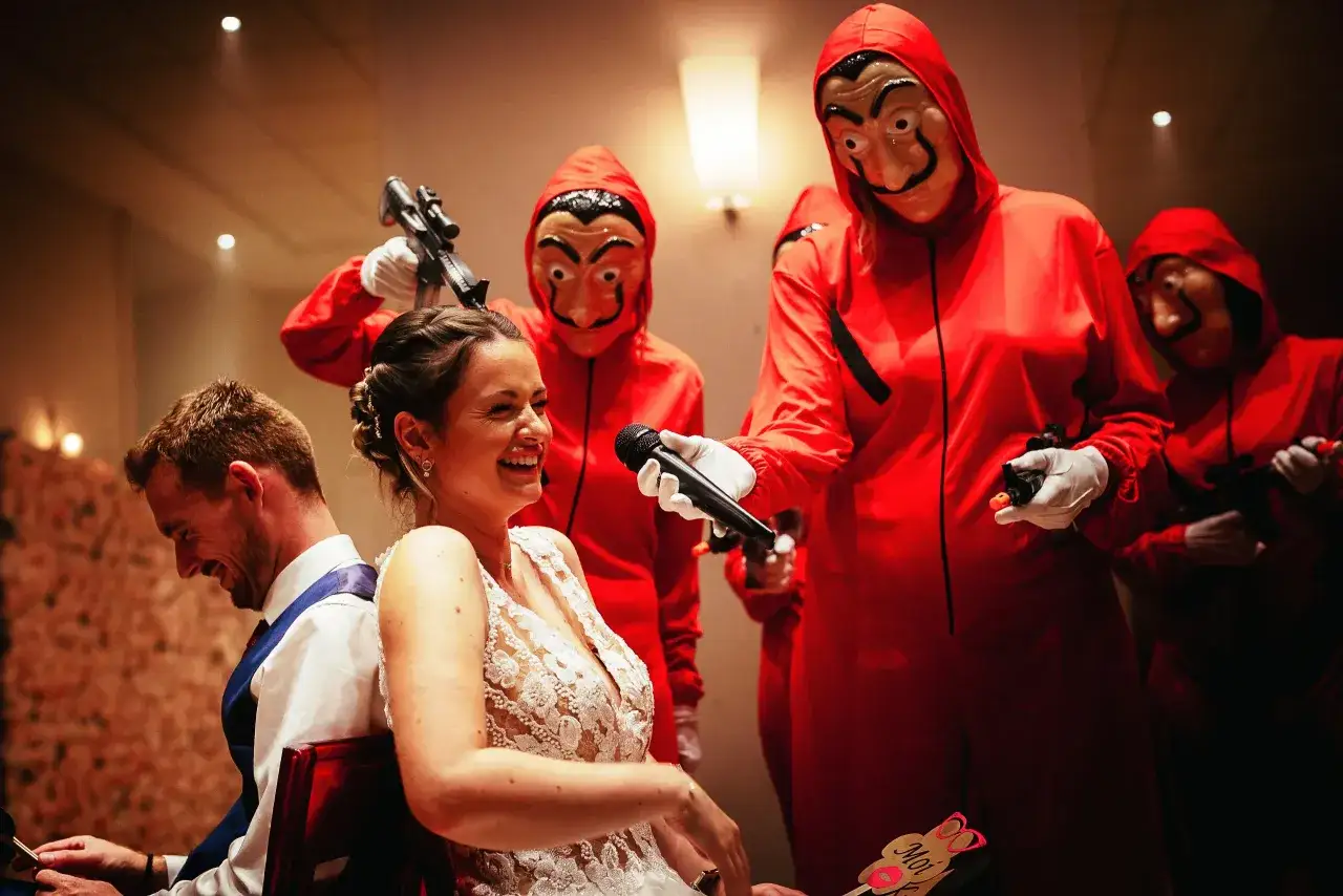 Une animation anniversaire de mariage inattendue : des invités masqués et costumés en rouge font une entrée surprise, micro et pistolets à la main, pour le plus grand bonheur des mariés.