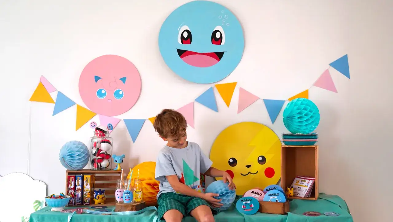 Un garçon décore une fête d'anniversaire sur le thème Pokémon. Des décorations DIY, comme des cercles de Pokémon et des guirlandes, ornent le mur.