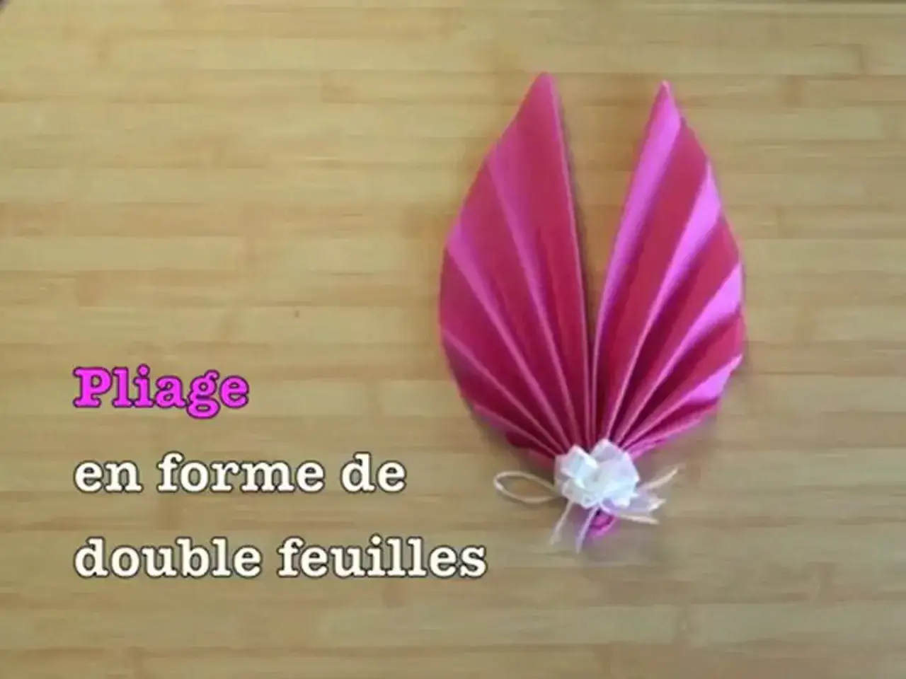 Pliage serviette palmier, une cr&eacute;ation &eacute;l&eacute;gante en forme de double feuilles, d&eacute;cor&eacute;e d'un n&oelig;ud blanc.