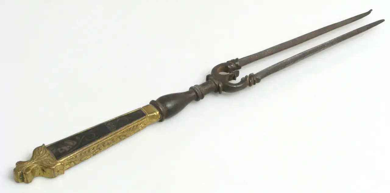 Une ancienne fourchette ornée, peut-être un indice sur qui a inventé la fourchette. Son manche est en bois sombre et orné de motifs dorés.