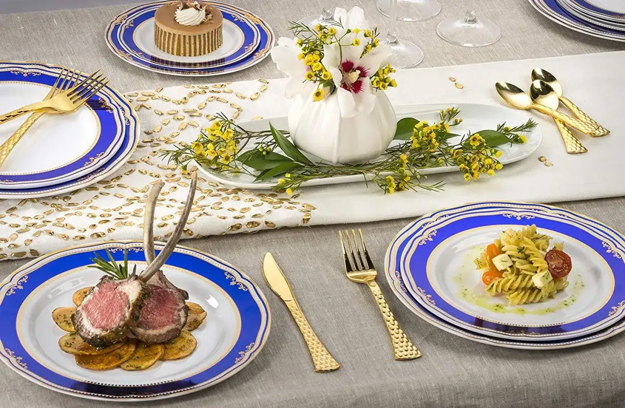 Un couvert de table élégant avec des assiettes bleues et dorées, des couverts dorés, un gigot d'agneau et un petit gâteau.
