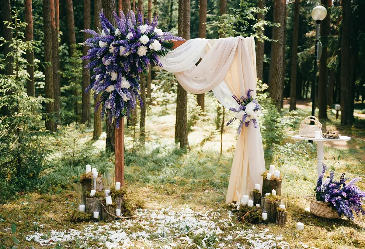Décoration d'une cérémonie laïque champêtre dans une forêt, avec un arche fleuri, des bougies sur des troncs et des pétales au sol.