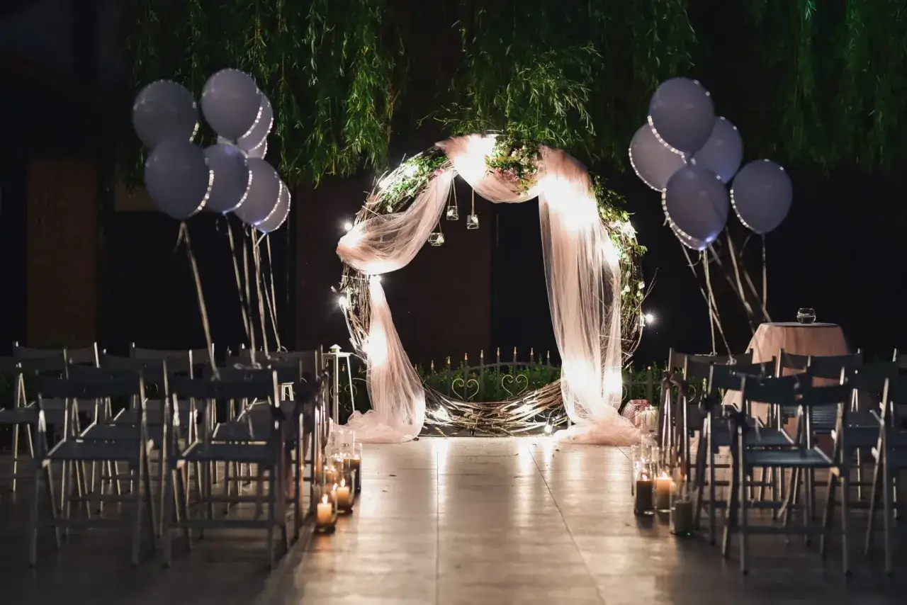 Allées de chaises éclairées par des bougies, arche de mariage ornée de lumières et de fleurs, ballons suspendus. Un décor féerique pour un thème mariage étoile.