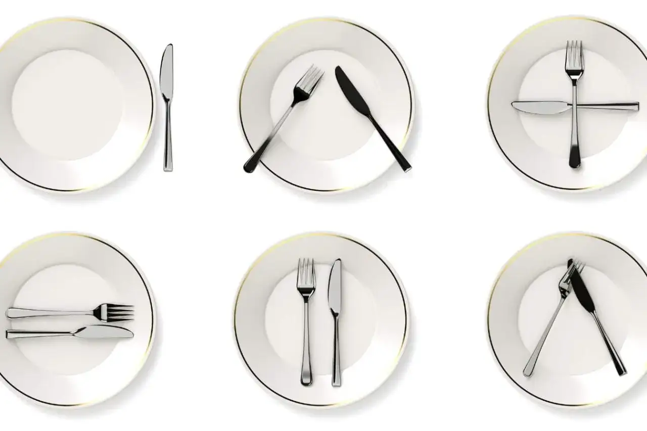 Six assiettes blanches avec des couverts disposés selon différentes positions des couverts à la fin du repas.