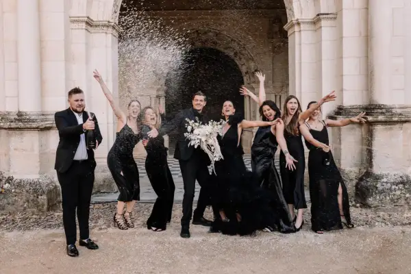 Un groupe joyeux célèbre un mariage noir et blanc, le marié ouvrant une bouteille de champagne sous une pluie de confettis.