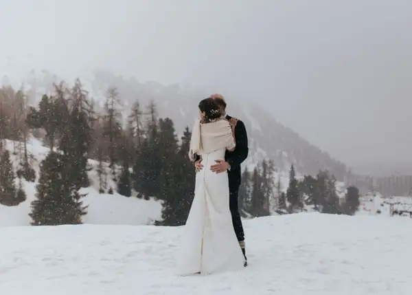 Un couple s'embrasse dans un paysage enneigé, un mariage thème montagne inoubliable.