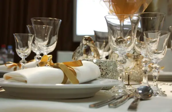 Service plat sur table avec des verres en cristal, des serviettes blanches nouées de ruban doré et des décorations scintillantes.