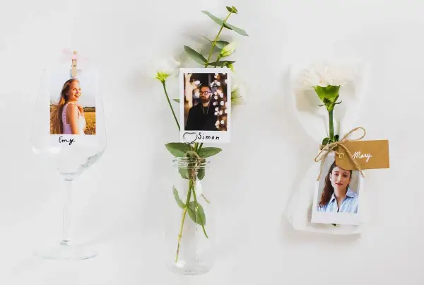 Marque place fleur : photos de invités (Emy, Simon, Mary) attachées à des fleurs et des verres, pour une décoration de table personnalisée.