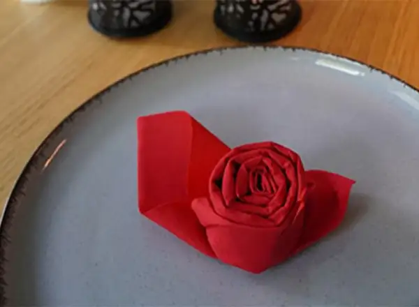Un pliage serviette papier en forme de rose rouge sur une assiette grise. Une touche d'élégance pour une table.