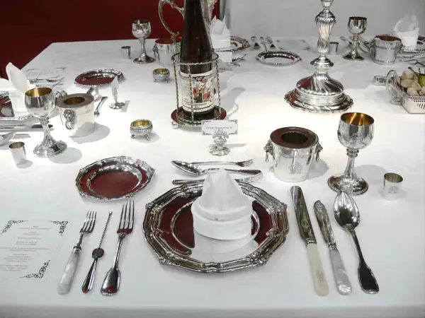 Une table dressée pour un service à l'anglaise, avec vaisselle en argent, verres, couverts et bouteille de vin.