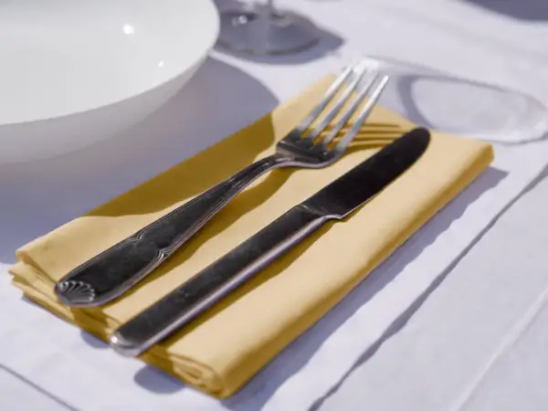 Un couteau et une fourchette reposent sur un noeud serviette de table jaune, prêt pour un repas.