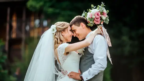 Un couple s'embrasse tendrement, le bouquet de la mariée rappelant une fête foraine. Un mariage plein de joie et d'amour.