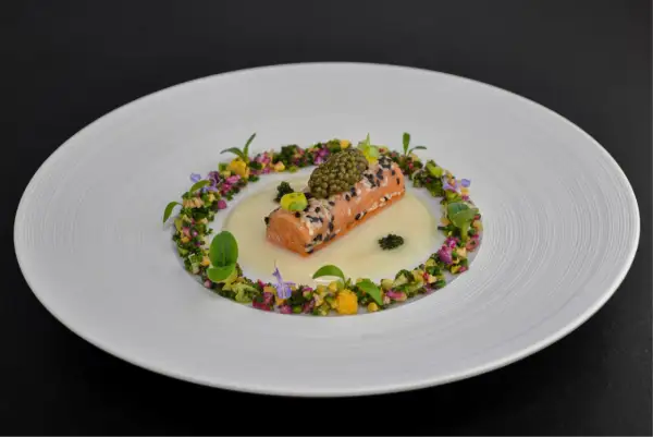 Un délicat pavé de saumon enrobé de sésame, surmonté de caviar, baignant dans une sauce onctueuse. Un plat qui pourrait faire partie d'un repas 7 services, orné de fleurs et de légumes croquants.