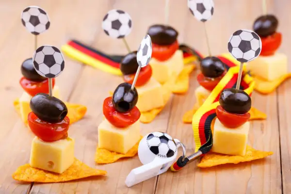 Décoration foot à faire soi même : brochettes de fromage, tomates et olives sur chips, ornées de mini ballons et de rubans aux couleurs allemandes.