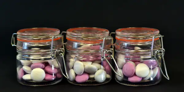 Trois bocaux en verre remplis de bonbons roses et blancs, une idée originale par quoi remplacer les dragées mariage.