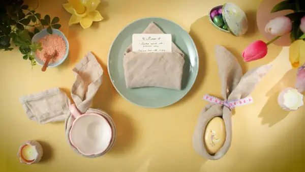 Jolie table de Pâques avec un pliage serviette bapteme en forme de lapin, des œufs décorés et des tulipes.