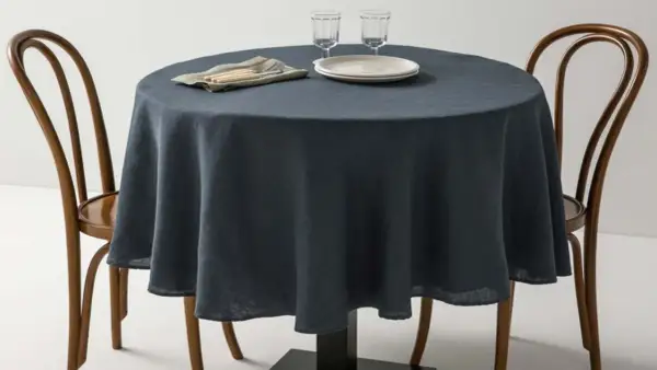 Table ronde avec nappe bleu nuit, deux chaises en bois et vaisselle. Une idée pour quel nappe choisir pour un dîner élégant.