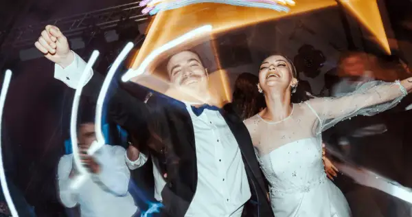 Un couple rayonnant danse joyeusement lors d'un mariage, peut-être celui d'un collègue de travail, sous des lumières festives.