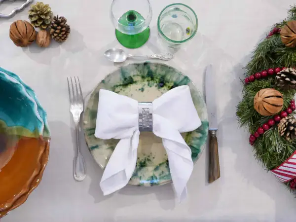 Une table dressée pour Noël avec un pliage serviette robe élégant, des pommes de pin et une guirlande festive.