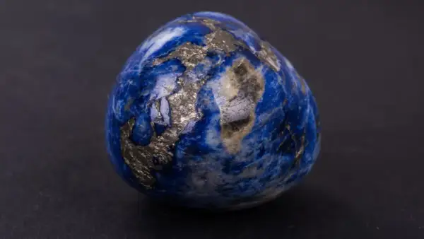 Un œuf en lapis-lazuli, rappelant les noces de saphir pour 56 ans de mariage, scintille de reflets dorés sur fond sombre.